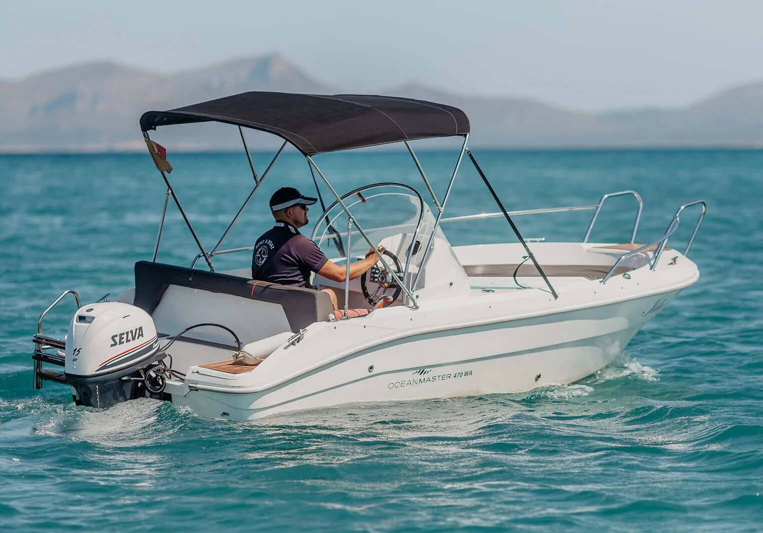 White Ocean Master open motorboat with a dark bimini top, underway with mountains behind